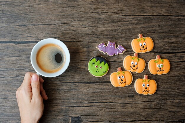 Mano sosteniendo la taza de café durante la comida divertida galletas de Halloween. Feliz día de Halloween, truco o amenaza, hola octubre, otoño otoño, concepto tradicional, fiesta y vacaciones