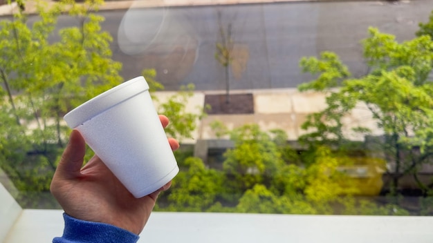 Una mano sosteniendo una taza de café frente a una ventana