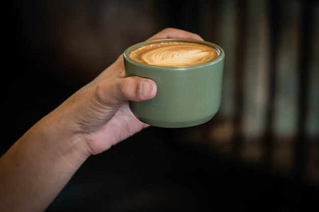 Mano sosteniendo una taza de café con leche vista superior que muestra arte latte en forma de hoja