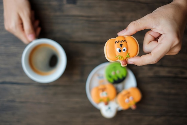 Mano sosteniendo una taza de café mientras come divertidas galletas de Halloween Feliz día de Halloween Truco o amenaza Hola Octubre otoño Otoño Fiesta tradicional y concepto de vacaciones