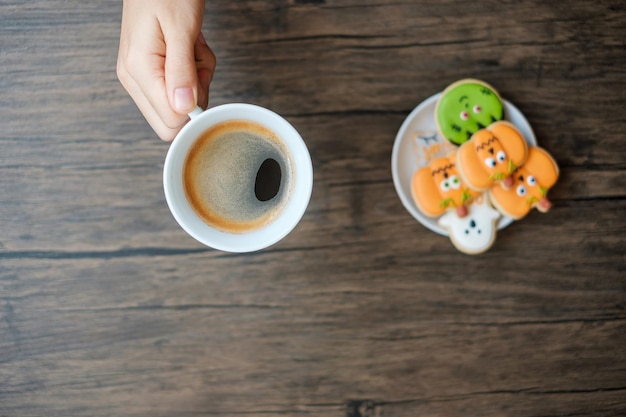 Mano sosteniendo una taza de café mientras come divertidas galletas de Halloween Feliz día de Halloween Truco o amenaza Hola Octubre otoño Otoño Fiesta tradicional y concepto de vacaciones