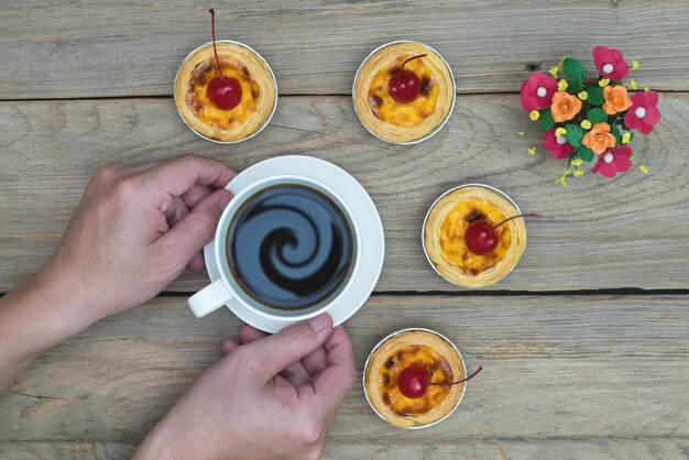 mano sosteniendo taza de café con tarta de huevo en la vista de la mesa de madera