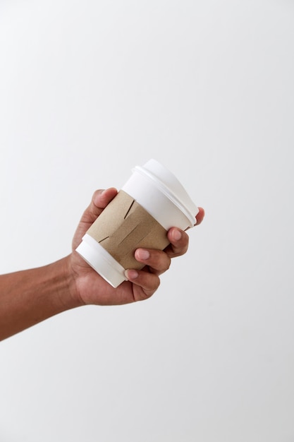 Mano sosteniendo una taza de papel de café aislada en la pared gris claro