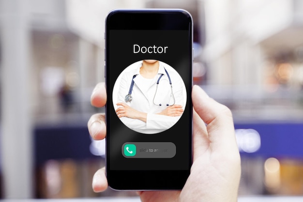 Mano sosteniendo el teléfono celular con una llamada entrante del médico sobre un fondo interior borroso Concepto de consulta a distancia