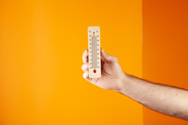 Foto mano sosteniendo un termómetro casero. temperatura del aire sobre un fondo naranja