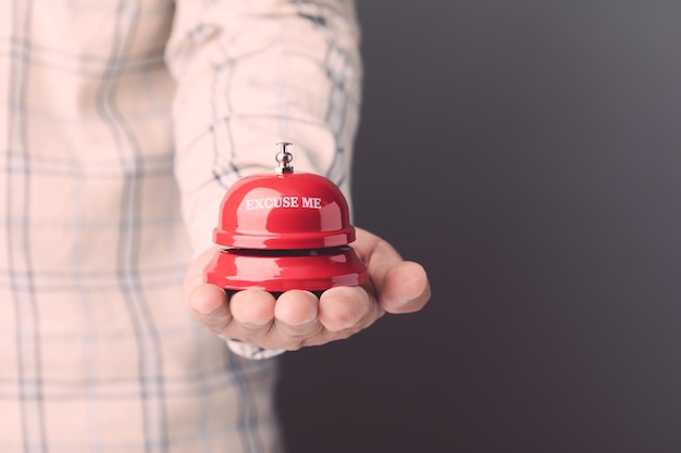 Mano sosteniendo el timbre de llamada rojo o el timbre de servicio en el fondo de la pared gris Para el concepto de publicidad de hotel o restaurante