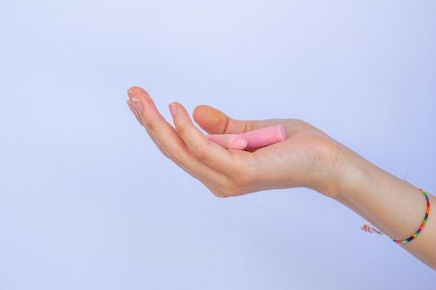 Mano sosteniendo tiza sobre fondo blanco aislado. Trozos de tiza rosa en una mano de mujer.