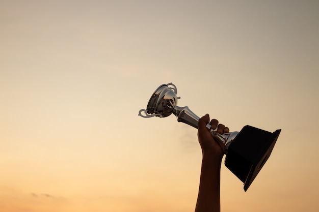 Foto mano sosteniendo un trofeo en la puesta del sol