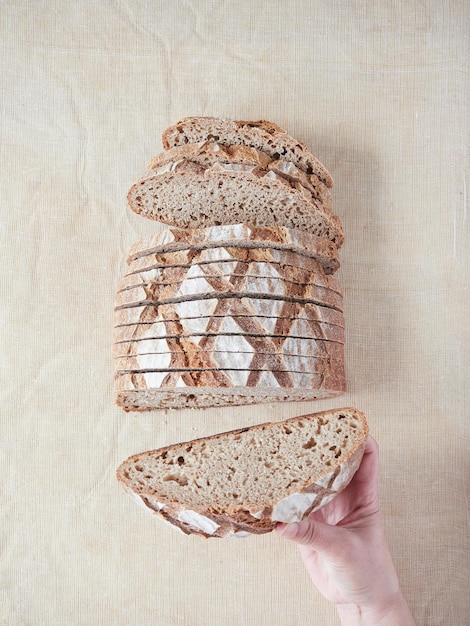 Mano sosteniendo un trozo de pan de masa madre artesanal que muestra el interior de miga de panal bien fermentado Vista superior sobre la superficie de lino de color crema