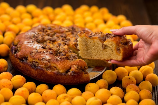 Mano sosteniendo un trozo de sabroso pastel de albaricoque sobre fondo de madera