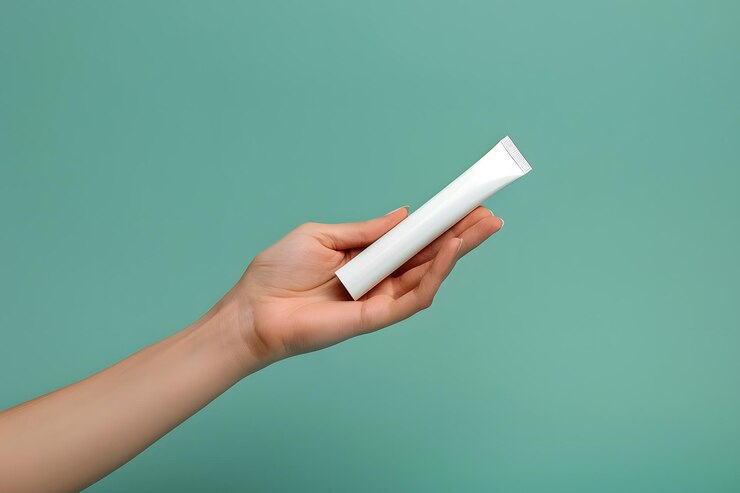 La mano sosteniendo un tubo de cosméticos blanco contra un fondo verde suave