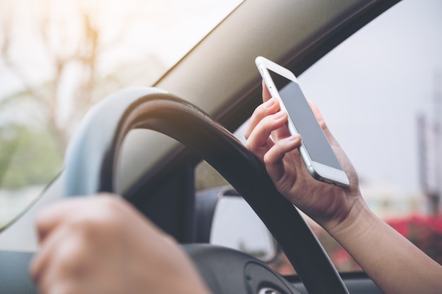 una mano sosteniendo y usando un teléfono móvil mientras conduce un automóvil en la carretera