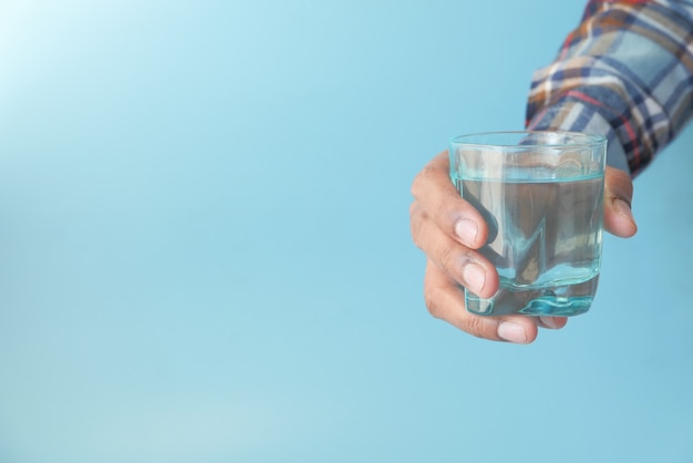 Mano sosteniendo un vaso de agua contra el fondo azul.