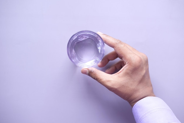 Mano sosteniendo un vaso de agua sobre fondo morado