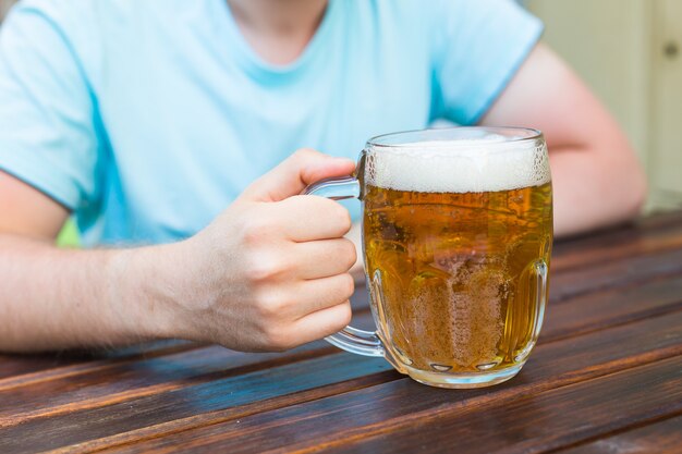 Mano sosteniendo un vaso de cerveza en la mesa de madera