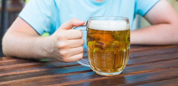 Mano sosteniendo un vaso de cerveza en la mesa de madera