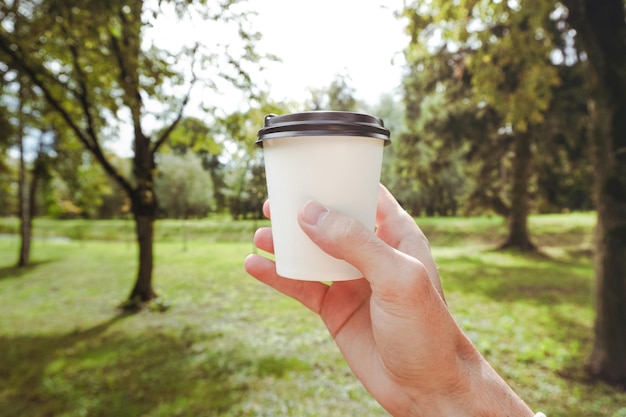 Una mano sosteniendo un vaso de papel Taza de papel blanco para café o té sobre fondo de hierba