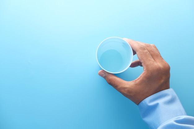 Mano sosteniendo un vaso de plástico de fondo azul.