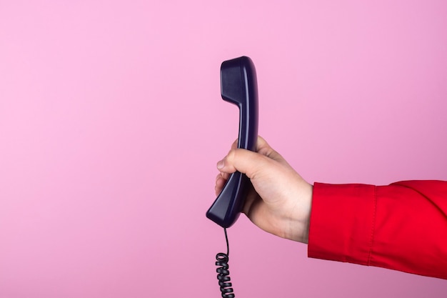 Mano sostiene un auricular de teléfono sobre un fondo rosa