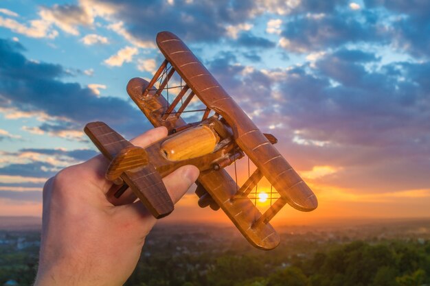 La mano sostiene el avión de madera en el fondo de una puesta de sol