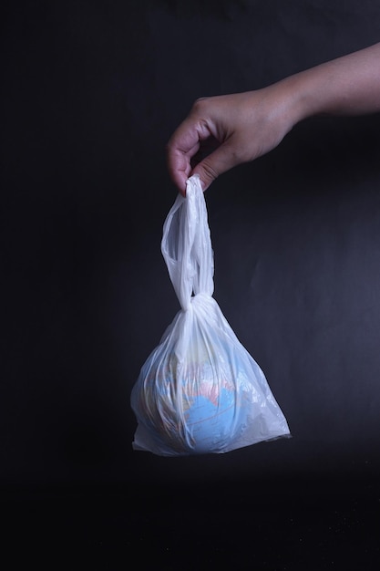 La mano sostiene una bolsa de plástico con el globo terráqueo del planeta en un fondo oscuro. El concepto de contaminación plástica.