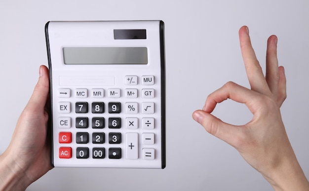 La mano sostiene la calculadora y muestra un gesto correcto sobre fondo gris