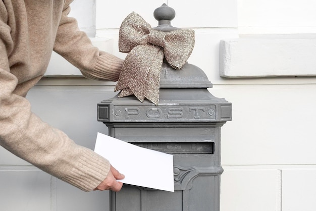 La mano sostiene una carta y la pone en un buzón antiguo cerca de la casa, entrega de la oficina de correos