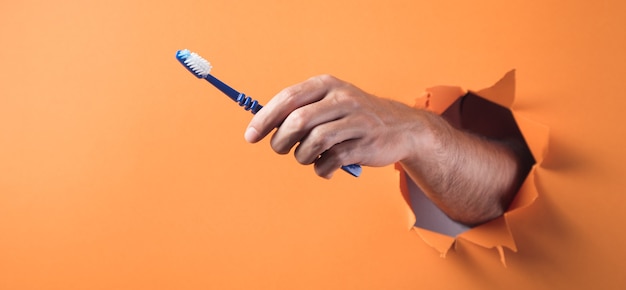 Mano sostiene un cepillo de dientes sobre un fondo naranja