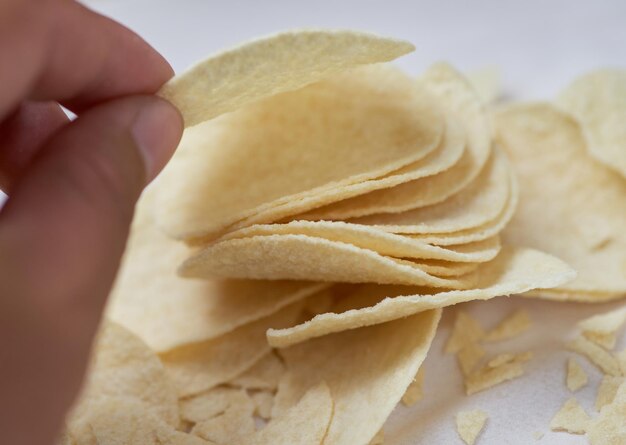 Una mano sostiene un chip de tortilla frente a un fondo blanco.