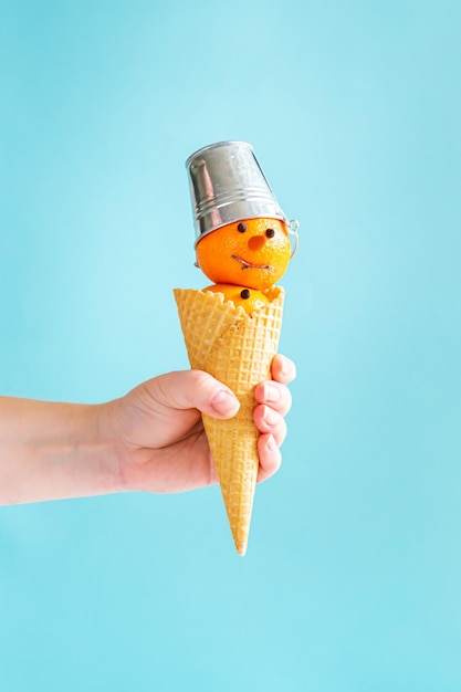 La mano sostiene un cono de galleta con un muñeco de nieve de mandarinaxA