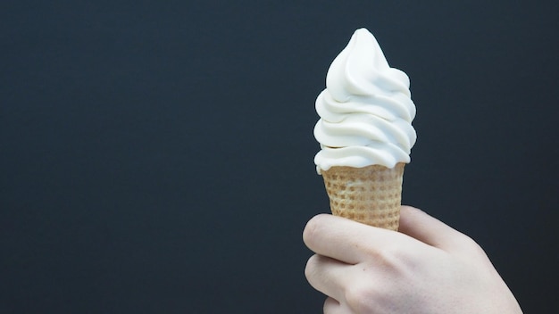 Foto la mano sostiene un cono de helado de softserve con un fondo negro