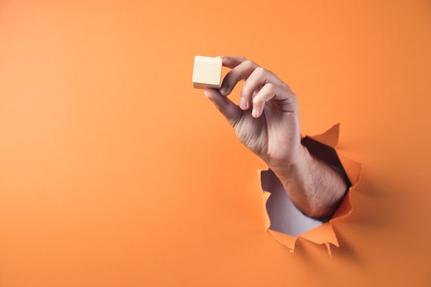 Mano sostiene el cubo de madera sobre fondo naranja