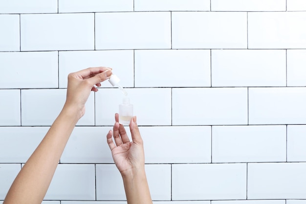 La mano sostiene el cuentagotas con aceite. Frasco abierto de producto cosmético natural sobre el fondo minimalista.