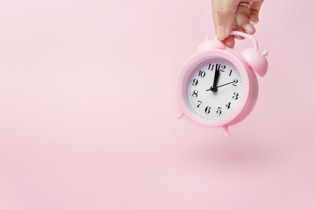 Una mano sostiene el despertador. Un concepto del tiempo y las nuevas tecnologías. Fondo rosa claro.