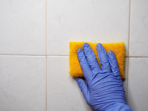 La mano sostiene una esponja contra una pared de azulejos