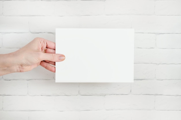 La mano sostiene el formulario en blanco blanco contra la pared de ladrillo Copiar espacio espacio de texto Información de la plantilla de diseño