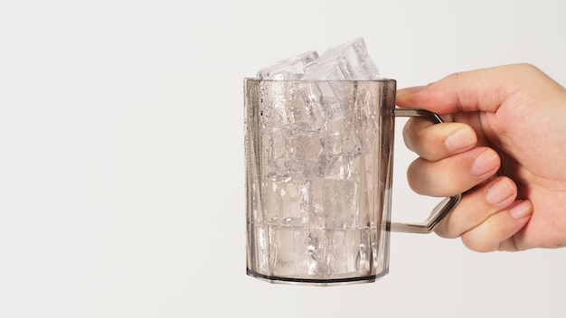 La mano sostiene un gloass de plástico con cubitos de hielo sobre fondo blancox9