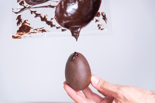 una mano sostiene un huevo con salsa de chocolate en él