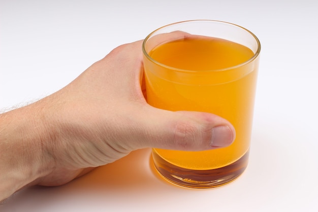 La mano sostiene el jugo en un vaso sobre un fondo blanco.