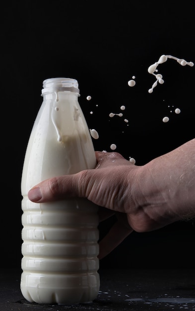 Mano sostiene la leche en una botella sobre un fondo negro con un toque