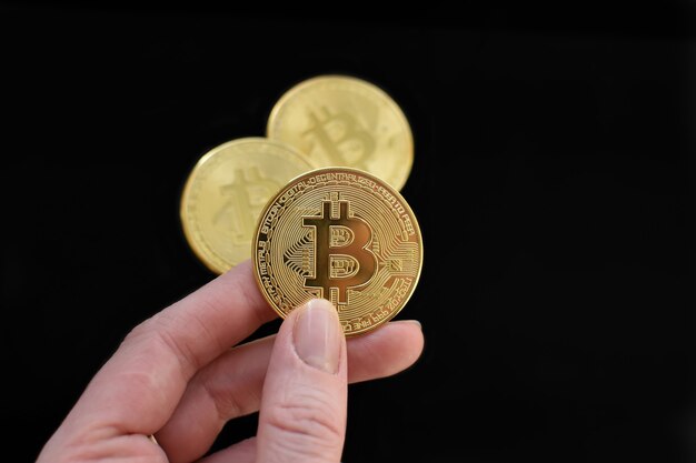 La mano sostiene la moneda Bitcoin de oro sobre fondo negro. Concepto: negocio, dinero electrónico. de cerca