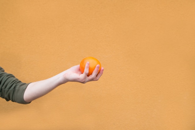 La mano sostiene una naranja en la pared de una pared naranja. Fruta del concepto