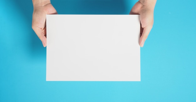 La mano sostiene el papel de tablero en blanco sobre fondo azul.