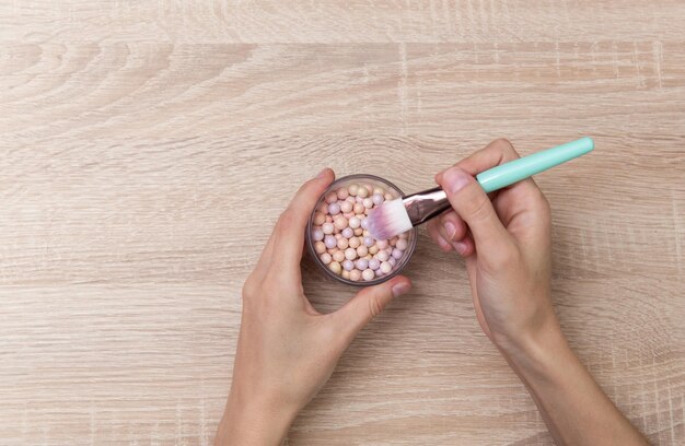 La mano sostiene un pincel de maquillaje y un frasco de bolas de polvo en la mesa