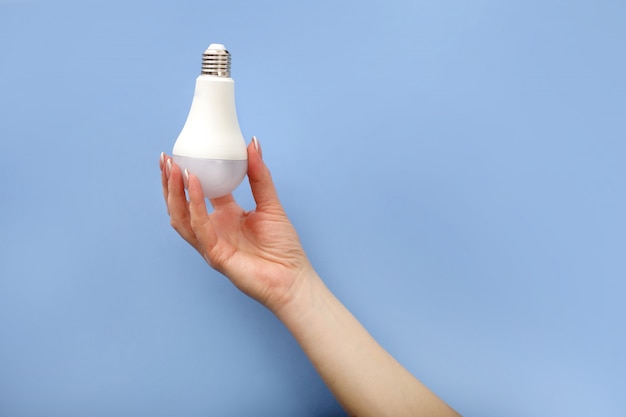 Foto una mano sostiene una tapa de bombilla led blanca sobre un fondo azul.