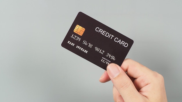 La mano sostiene una tarjeta de crédito negra aislada en un fondo gris