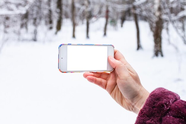 La mano sostiene el teléfono inteligente con pantalla recortada en invierno