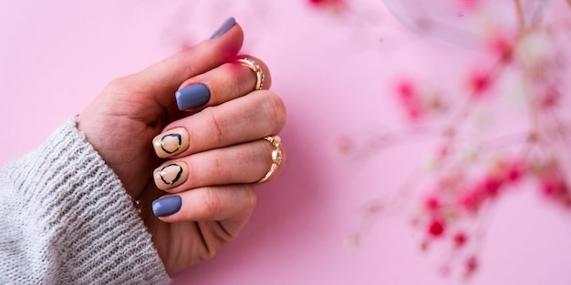 Foto mano en suéter y flores rosadas con uñas de manicura modernas. mano femenina. hermosa manicura glamorosa. concepto de salón de manicura. esmalte de uñas de cerca.