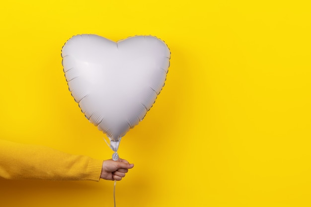 Mano sujetando ballon en forma de corazón sobre fondo amarillo, concepto de vacaciones con amor