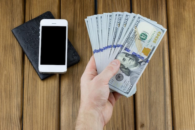 Mano sujetando billetes de dólar con smartphone